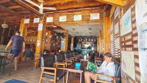 A restaurant with wooden interior, tables and chairs, and a person walking. - Koh Rong Home Stay (Sihanoukville)