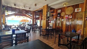 A restaurant with wooden furniture, a view of the sea, and a wooden wall with food pictures. - Koh Rong Home Stay (Sihanoukville)
