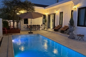 Ein Swimmingpool mit Liegestühlen und Sonnenschirm, umgeben von einer Terrasse mit Tisch und Stühlen.