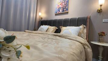 A hotel room with a large bed, a headboard, a bedside table with a lamp, and a painting on the wall.