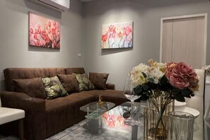A living room with a brown sofa, a glass coffee table, and a vase with flowers. - ChillTime (Chiang Rai)