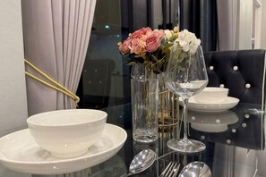 A dining table set with white plates, bowls, and clear glassware, accompanied by a vase with flowers. - ChillTime (Chiang Rai)