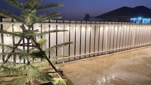 A palm tree in the foreground, a lighted fence, and a building with lights in the background. - ChillTime (Chiang Rai)