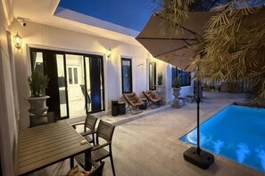 Una casa moderna con piscina, mobiliario exterior y un patio cubierto.