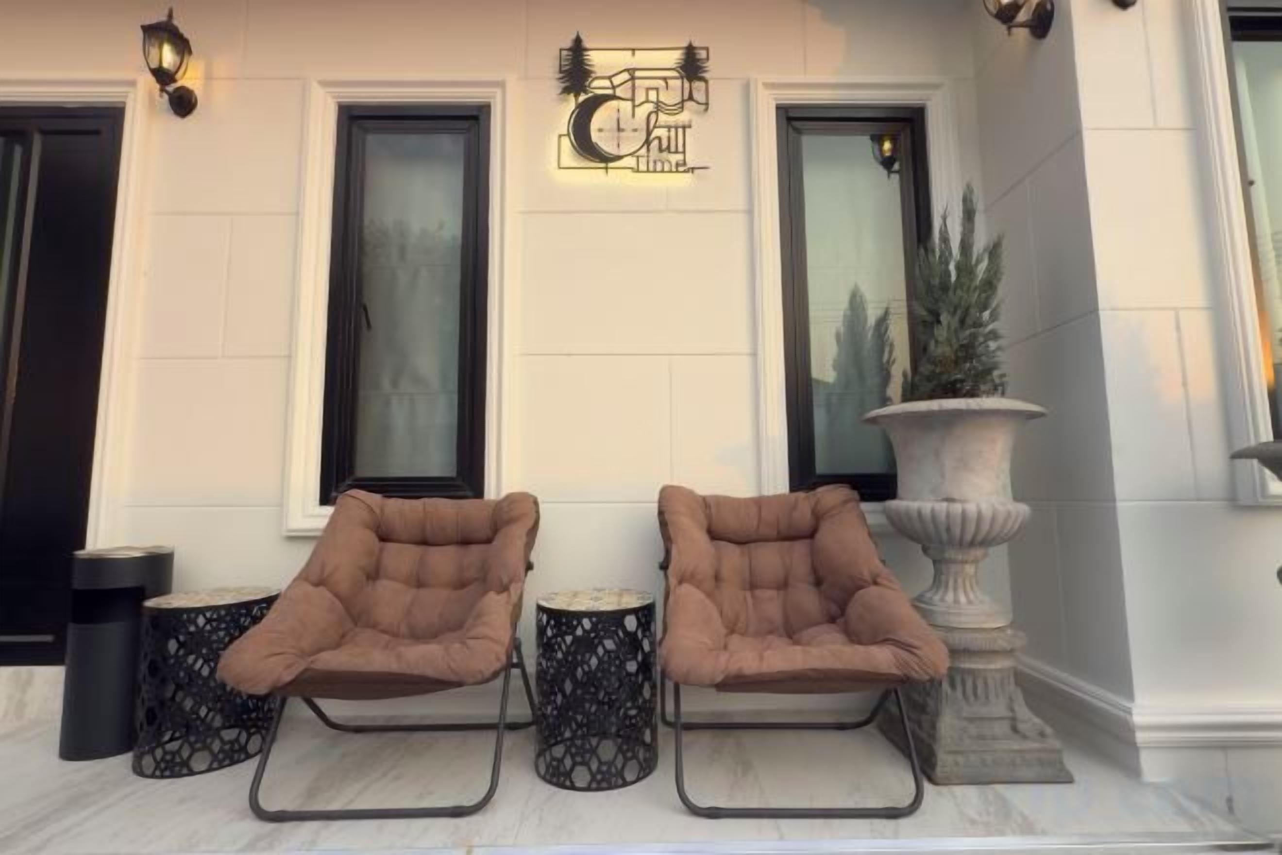 A set of three brown lounge chairs with metal frames and black patterned footrests, positioned on a marble floor in front of a building with large windows and a decorative wall-mounted sign.