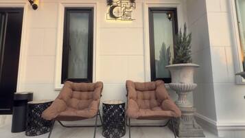 A set of three brown lounge chairs with metal frames and black patterned footrests, positioned on a marble floor in front of a building with large windows and a decorative wall-mounted sign.
