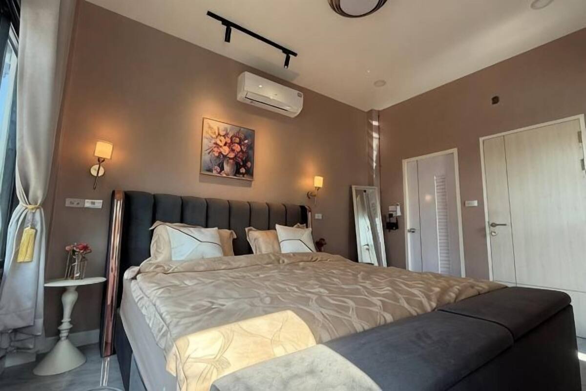 A bedroom with a bed, bedside tables, a mirror, and an air conditioning unit.