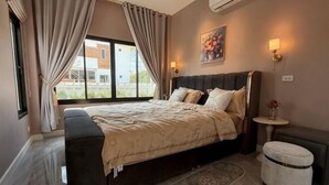 A bedroom with a bed, a bedside table, a lamp, a bench, and a window with curtains. - ChillTime (Chiang Rai)