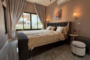 A bedroom with a bed, a bedside table, a lamp, a bench, and a window with curtains. - ChillTime (Chiang Rai)