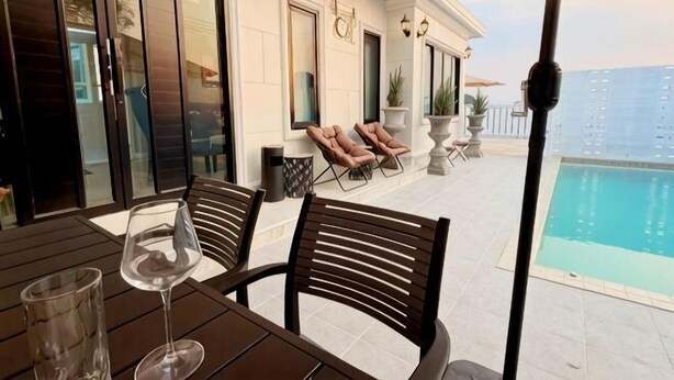 An outdoor patio with a table, chairs, and a glass of wine. There is a pool in the background and a view of the ocean. - ChillTime (Chiang Rai)