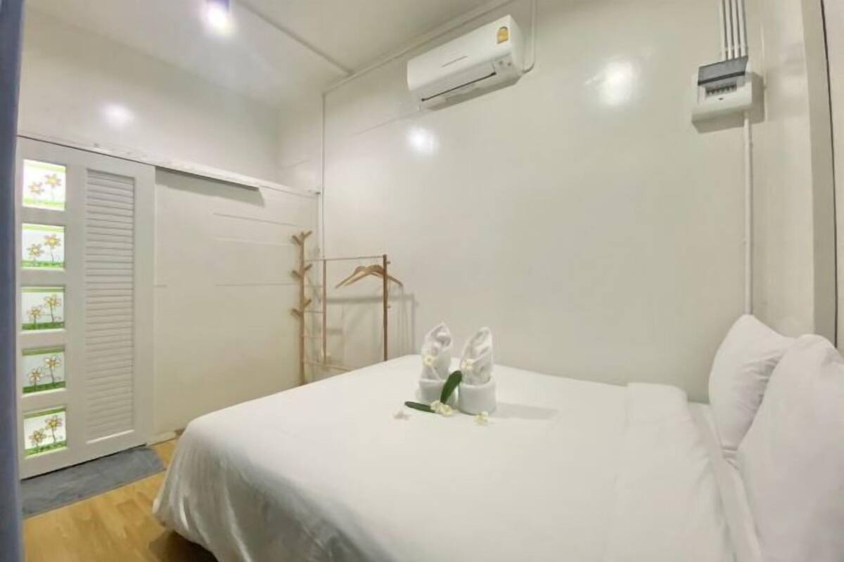 Une chambre d’hôtel avec un lit, des murs blancs, un appareil de climatisation et une porte avec une fenêtre.
