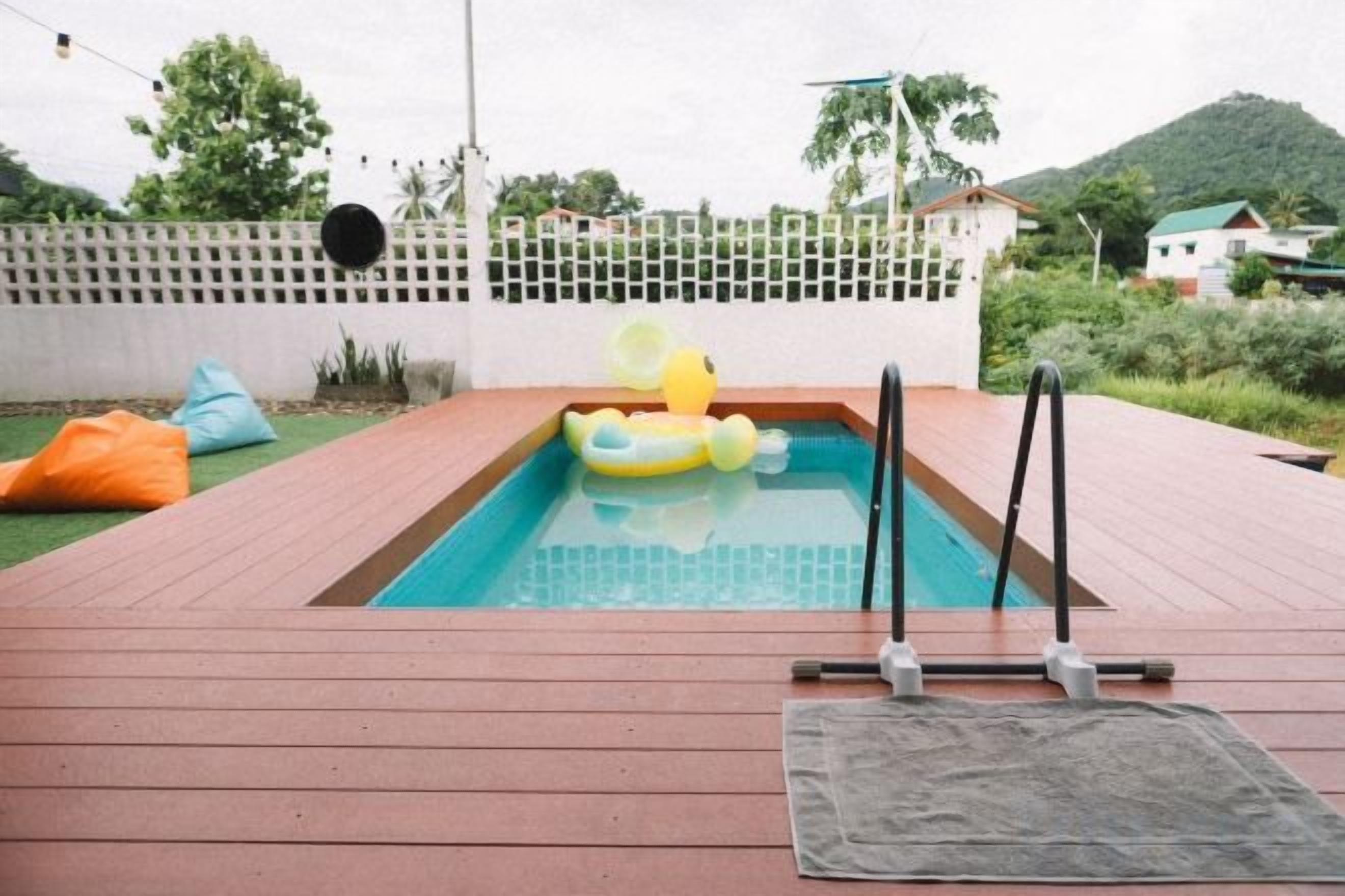A swimming pool with a yellow inflatable duck, surrounded by a wooden deck and a white fence.