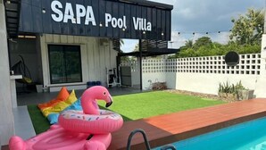 Un espace piscine agrémenté d’un flamant rose gonflable, d’un salon au bord de la piscine et d’un bâtiment portant l’inscription « SAPA Pool Villa ».