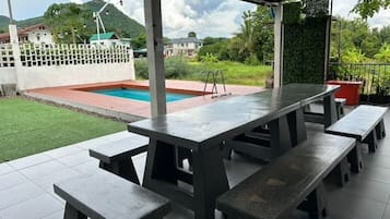 A covered outdoor area with a pool, picnic tables, and a view of the surrounding landscape.