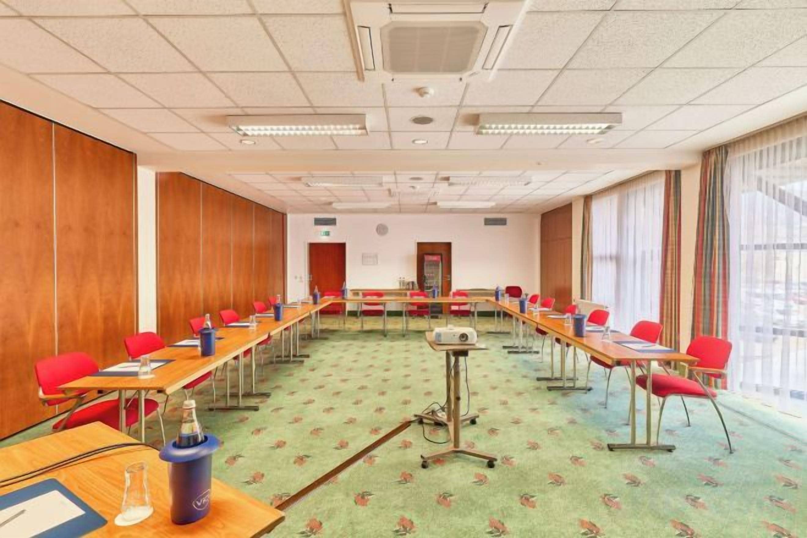 Un salón de conferencias con largas mesas y sillas, un proyector y piso alfombrado.