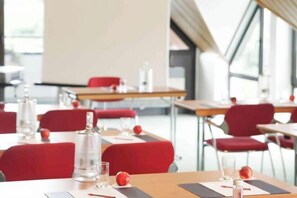 Un comedor moderno con mesas, sillas rojas y vasos de vidrio transparente.