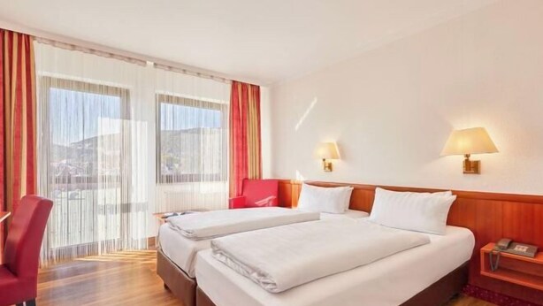 Ett hotellrum med två sängar, ett skrivbord, en stol och ett fönster med gardiner.