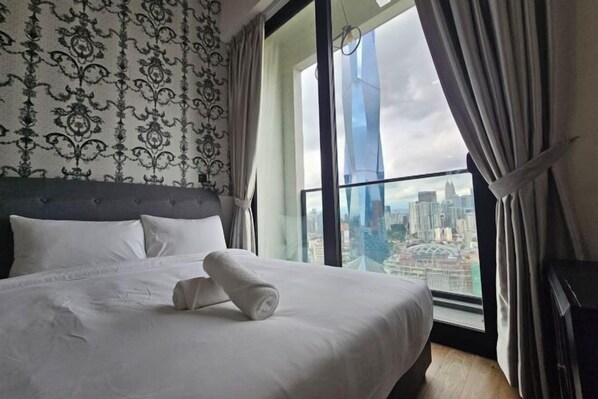 A hotel room with a large bed, a view of the city through a large window, and a patterned wallpaper.