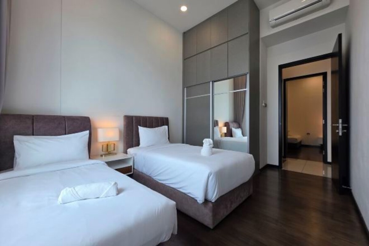 Een hotelkamer met twee bedden, een nachtkastje, een spiegel en een deur die naar een andere kamer leidt.
