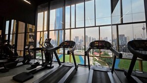 Une salle de sport équipée de tapis de course et d’appareils d’exercice, avec de grandes fenêtres offrant une vue sur la ville.