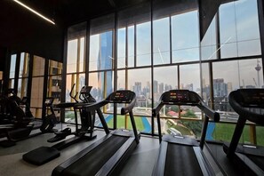 Ein Fitnessstudio mit Laufbändern und Trainingsgeräten, große Fenster mit Blick auf die Stadt.