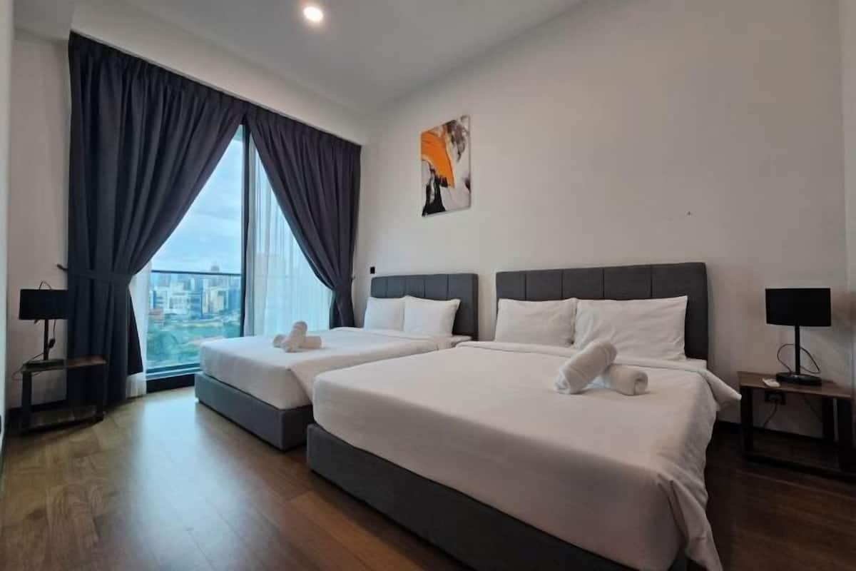 Une chambre d’hôtel avec deux lits, une grande fenêtre avec des rideaux, une vue sur la ville et un tableau au mur.
