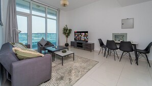 A modern living room with a sofa, coffee table, TV, and dining area. - Lux JVT Resort Pools Spa Gym Kids Play (Dubai)