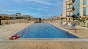 A rooftop pool with blue water, surrounded by lounge chairs and a lifebuoy. - Lux JVT Resort Pools Spa Gym Kids Play (Dubai)