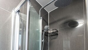 A shower with a glass door, a handheld showerhead, and a wall-mounted faucet. - Modern Studio w/private Kitchen, Bathroom & Garden (Basildon)