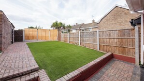 A backyard with a green lawn, brick pathway, wooden fence, and brick walls. - Modern Studio w/private Kitchen, Bathroom & Garden (Basildon)