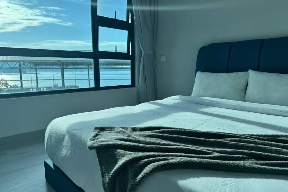 A bed with a view of a body of water through a window.