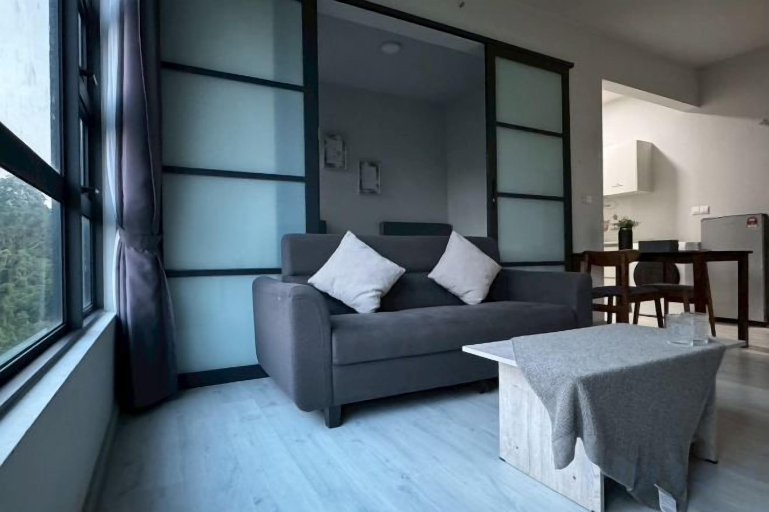 A modern living room with a sofa, a coffee table, and a view through a large window.