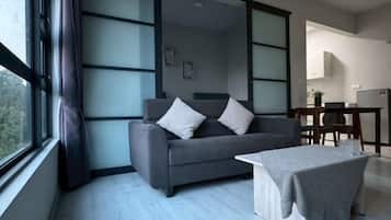 A modern living room with a sofa, a coffee table, and a view through a large window.