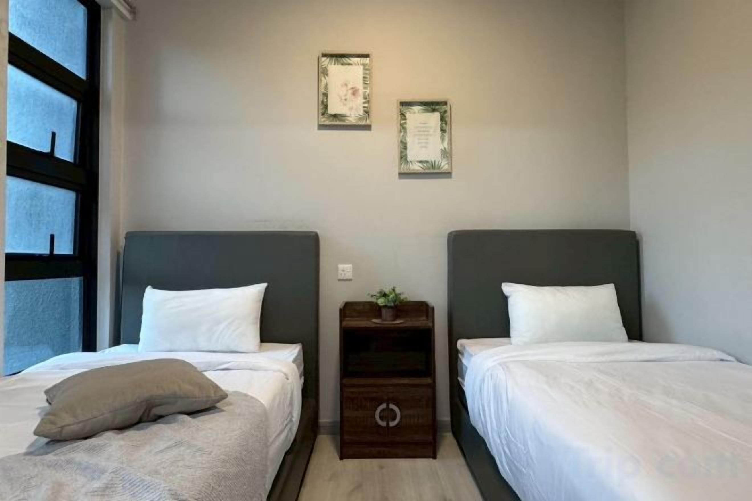 Quarto de hotel com duas camas, uma mesinha com uma planta e dois certificados emoldurados na parede.