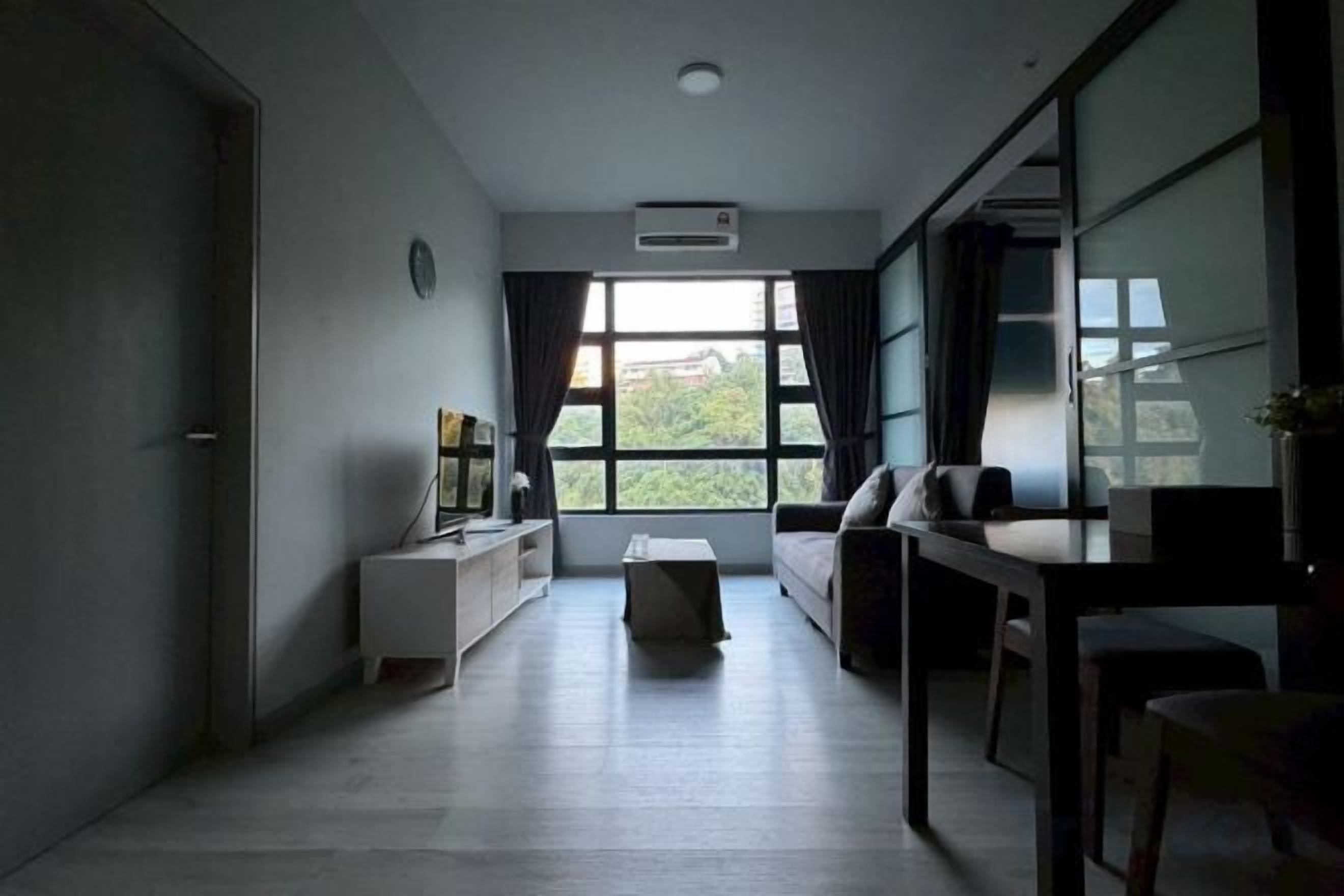 Uma sala de estar moderna com sofá, mesa de centro e suporte para TV. Há uma janela grande que oferece luz natural e vista para o exterior.