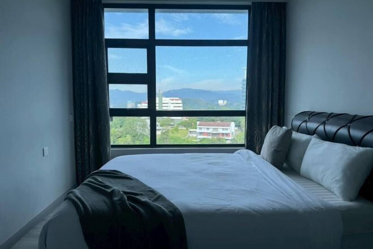 A hotel room with a large window, a bed, and a view of buildings and mountains.
