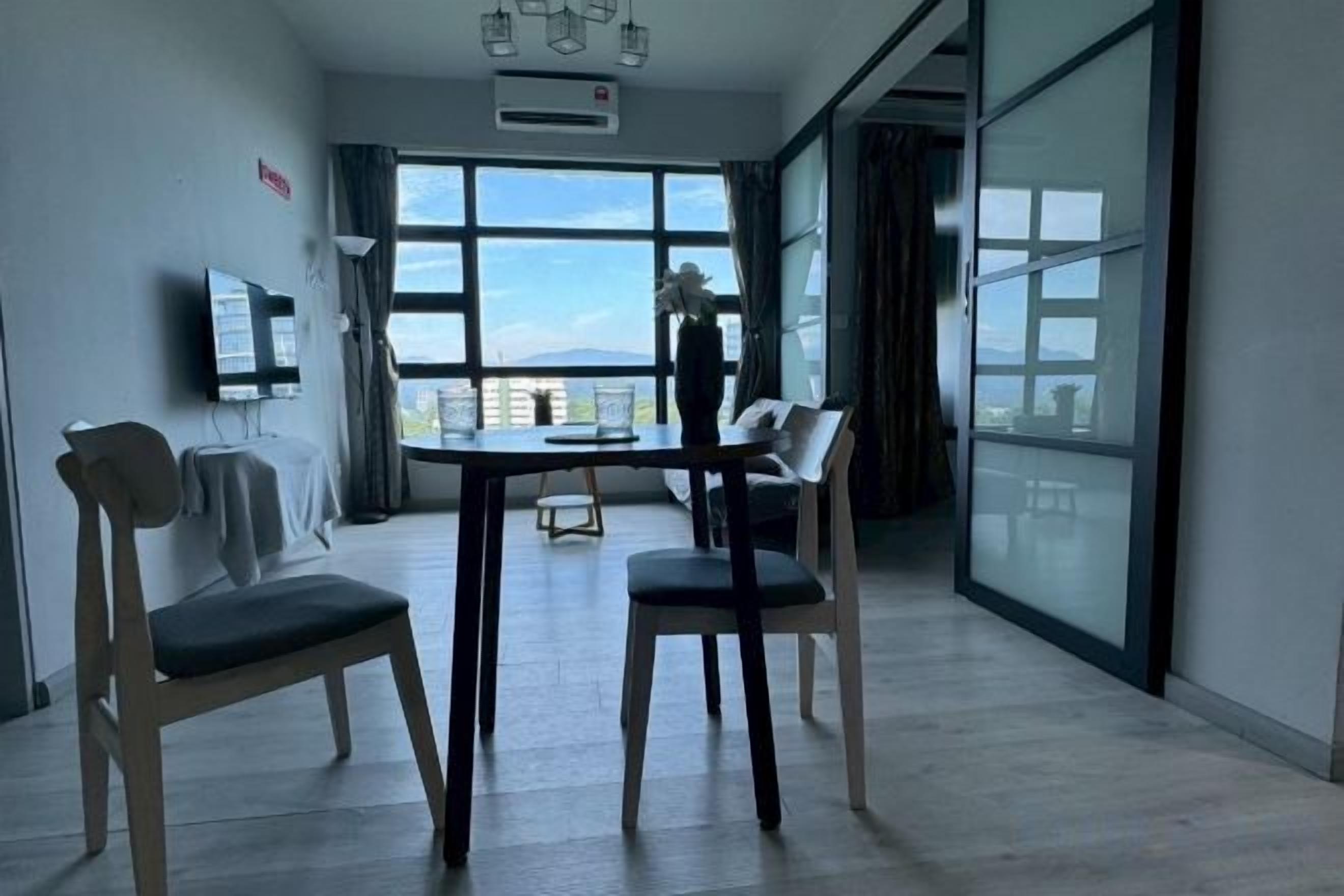 A modern hotel room with a large window, a flat-screen TV, and a dining area with chairs.