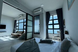 Habitació d'hotel moderna amb un llit, zona de seients amb un sofà i cadires, grans finestres i un aparell d'aire condicionat.