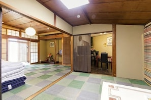 A traditional Japanese room with tatami flooring, a tatami mat in the center, a wooden ceiling, and a sliding door leading to another room.