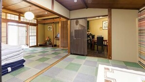 A traditional Japanese room with tatami flooring, a tatami mat in the center, a wooden door, and a view of a dining area. - -W- Vacation Rental (Nagoya)