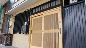 A building with a beige facade, a large beige door with vertical slats, and a black awning. - -W- Vacation Rental (Nagoya)