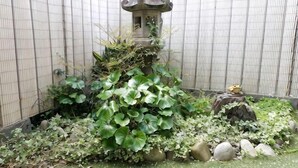 A stone lantern, a rock, and a statue in a garden with a wire fence. - -W- Vacation Rental (Nagoya)