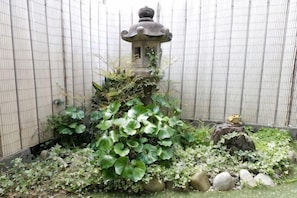 A stone lantern, a rock, and a statue in a garden with a wire fence. - -W- Vacation Rental (Nagoya)