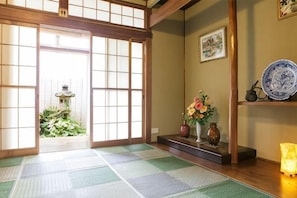 A traditional Japanese room with tatami flooring, a shoji screen door, a small garden, and a shelf with decorative items. - -W- Vacation Rental (Nagoya)