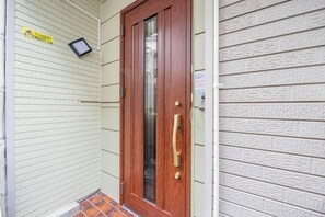A wooden door with a glass panel and a brass handle, a small sign above it, and a tiled entrance area. - Ikebukuro 5min｜10Guests｜Family House｜5BR (Tokyo)
