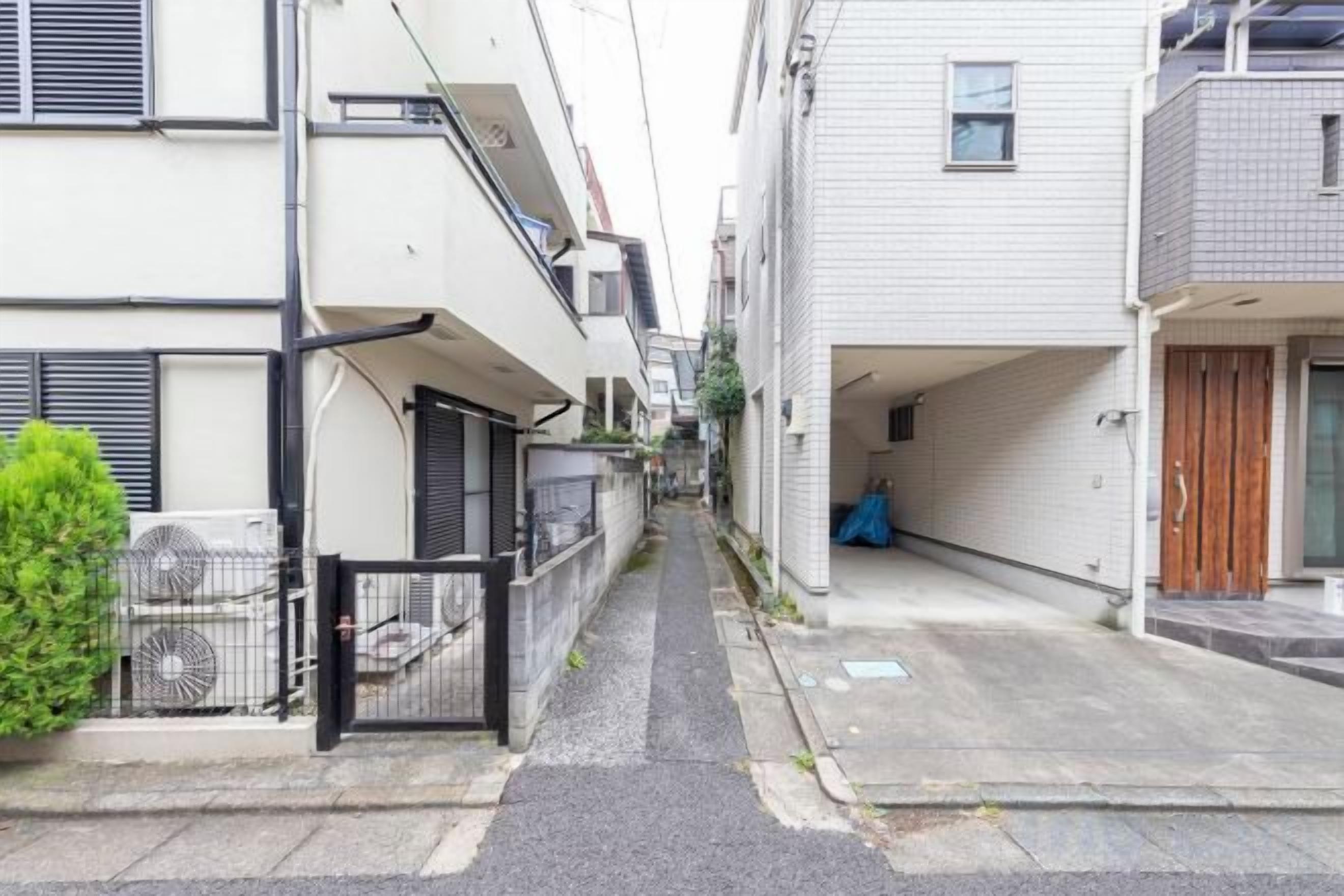 A narrow residential street with a white building on the left and a grey building on the right.
