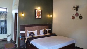 Una camera d'albergo con un letto, un comodino, una lampada a parete, una ventola a soffitto e una finestra con tende.