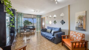 Ein Wohnzimmer mit einer Couch, einem Holzstuhl, einem Esstisch mit Stühlen und einem großen Fenster.
