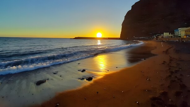Ein Strand mit Sonnenuntergang, Wellen und einer Klippe.