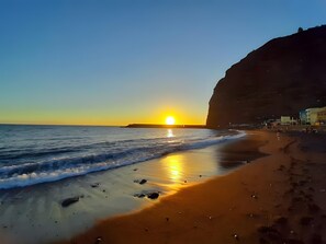 Una playa con atardecer, olas y un acantilado.